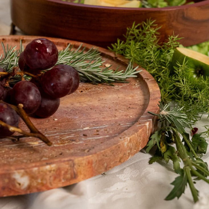 Elevated red traventine marble serving plate on three rounded legs, defined by natural veining. 